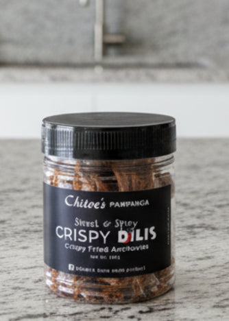 A clear plastic jar of Chito's Pampanga Sweet & Spicy Crispy Dilis crispy fried anchovies, featuring a black lid and a black label with white text, set against a plain white background.